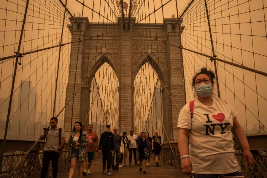 Citygoers wearing face coverings as they walk across the Brooklyn Bridge during the peak of the orange fog on Wednesday afternoon. Credit to Dave Sanders of The New York Times.